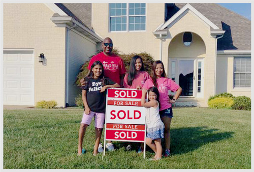 A family gathered around a sold sign in front yard of new home