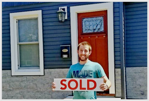 Man in front of new home holding a sold sign